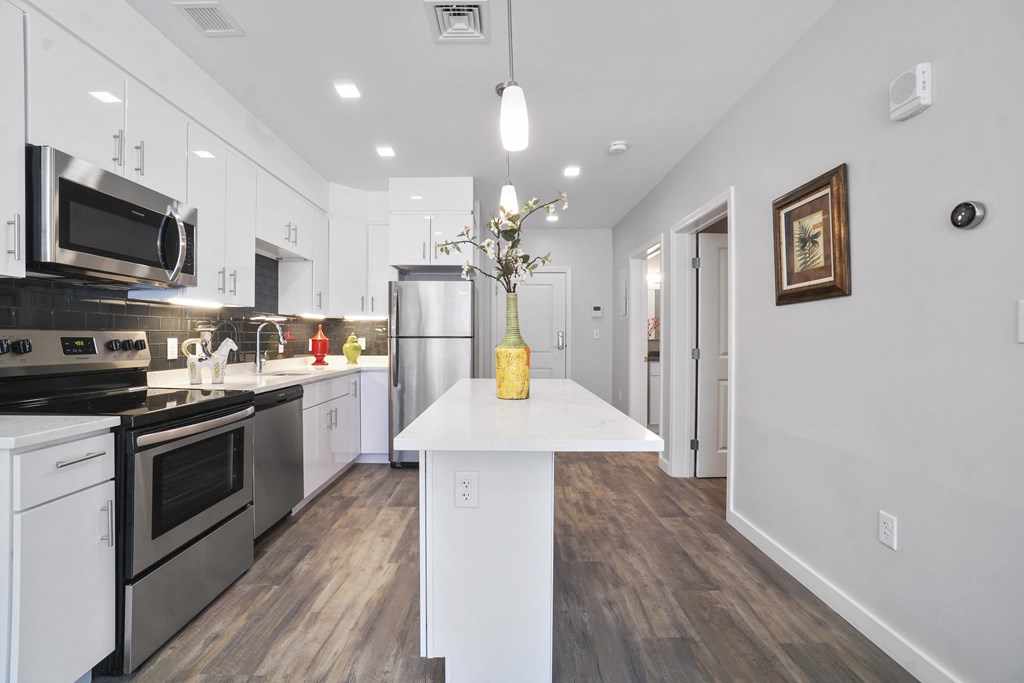 a kitchen with white cabinetry and a large white island with a yellow vase with flowers