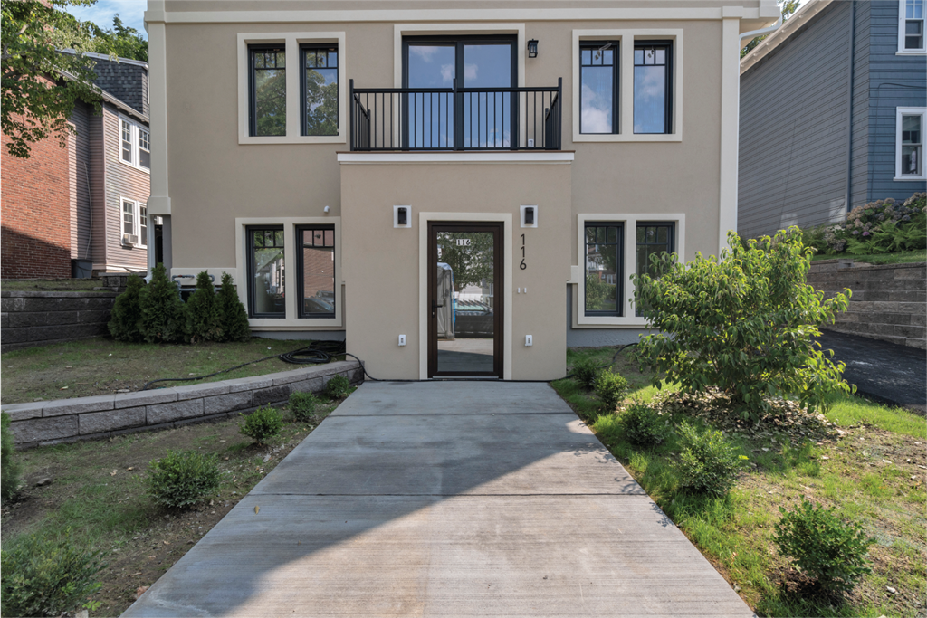 the front of a tan house with a driveway and a balcony