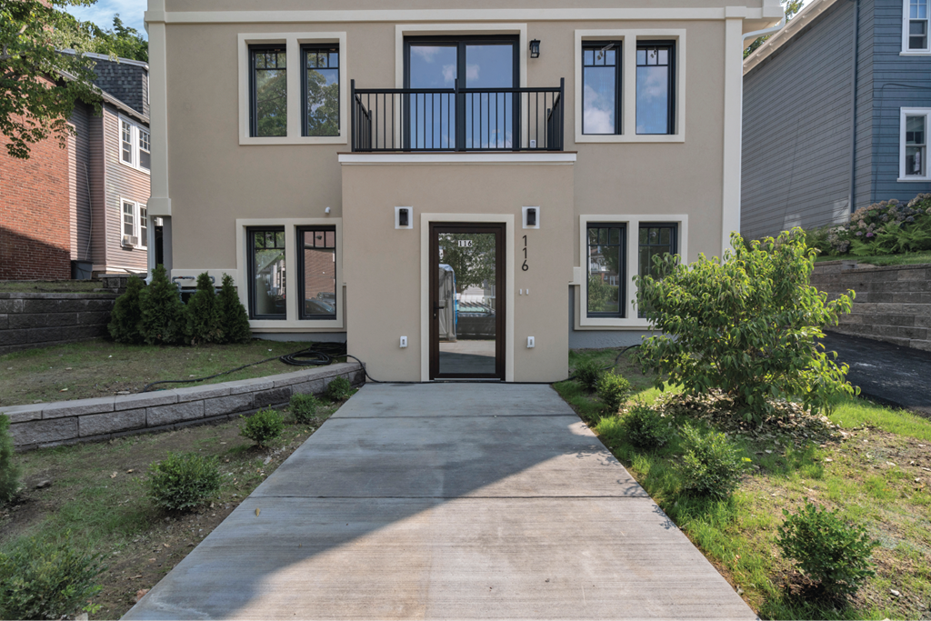 the front of a tan house with a driveway and a balcony