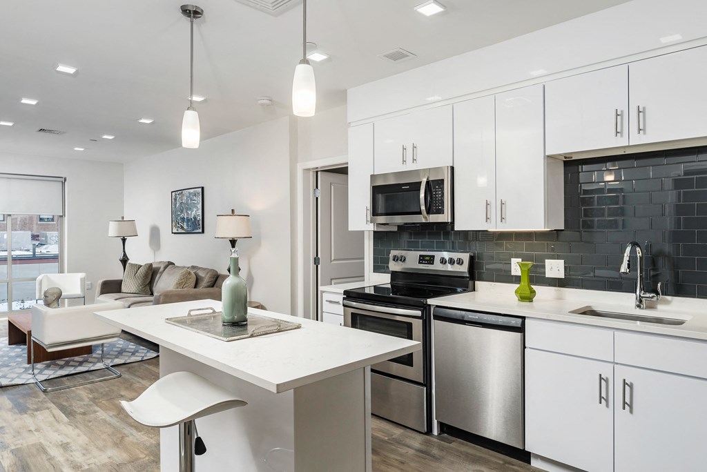 an open kitchen and living room with white cabinets and stainless steel appliances