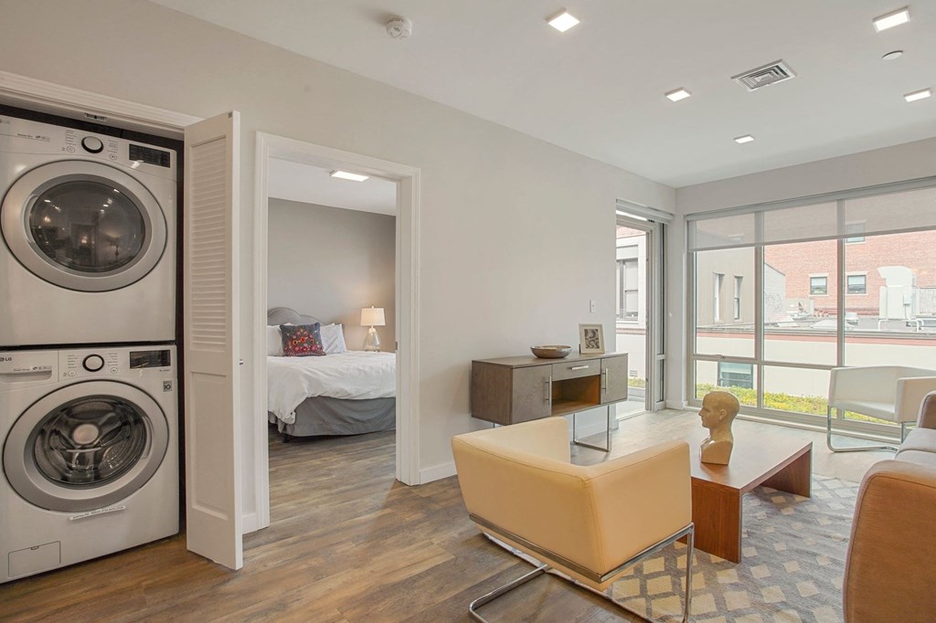 a living room with a washing machine and a bedroom with a bed