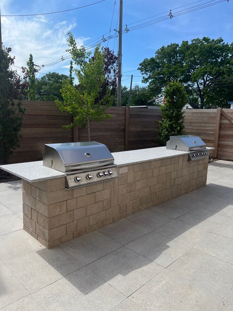 a brick outdoor kitchen with two grills in a backyard