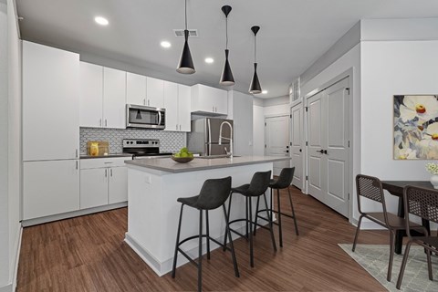 A kitchen with white cabinets and a white island with three black barstools.