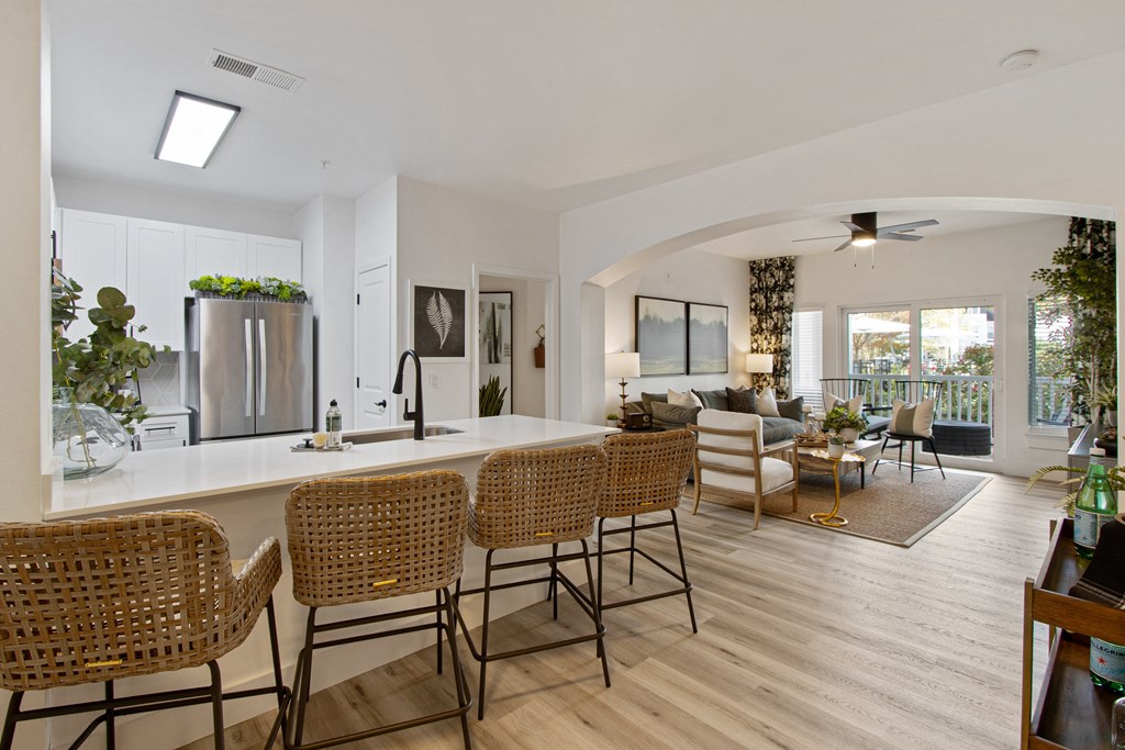 the kitchen and living room of a house with a large white counter and bar chairs