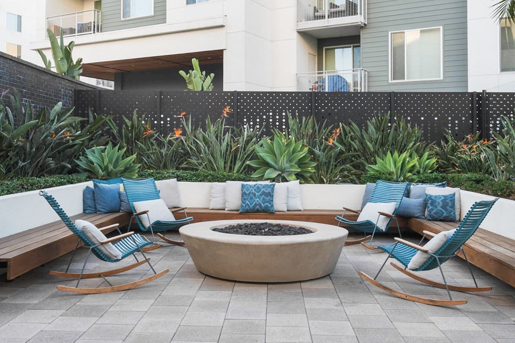 A patio with a fire pit surrounded by chairs and plants.
