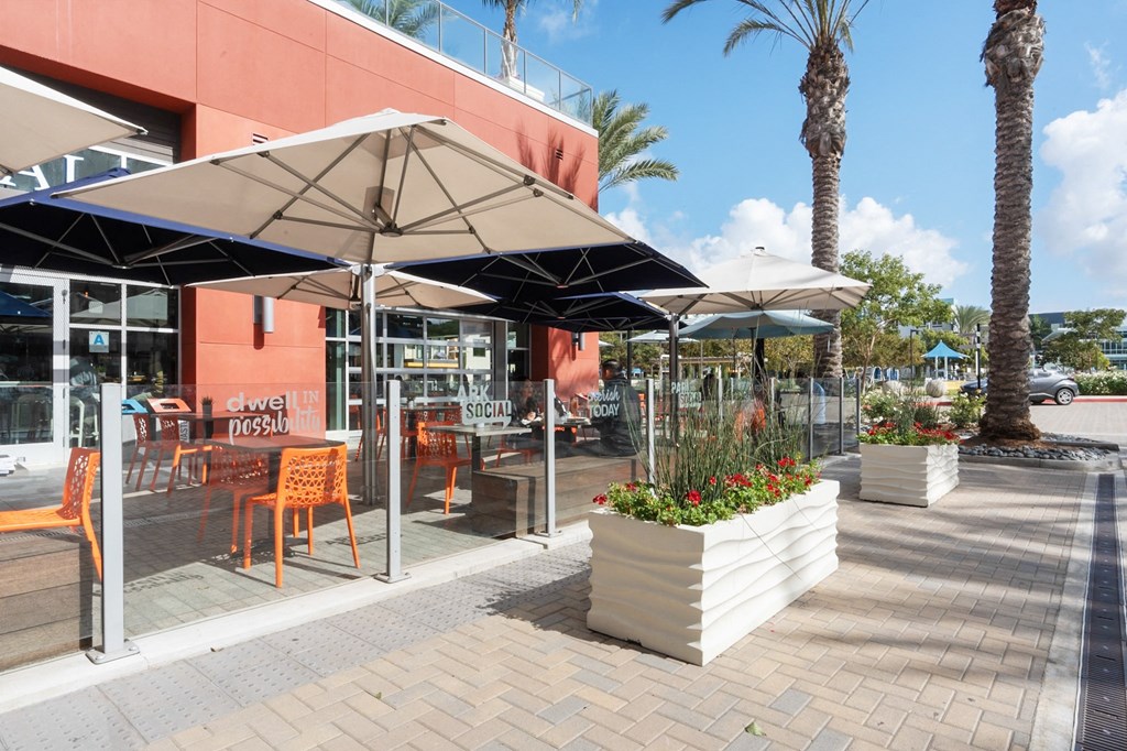 A sunny day at a cafe with orange chairs and umbrellas.