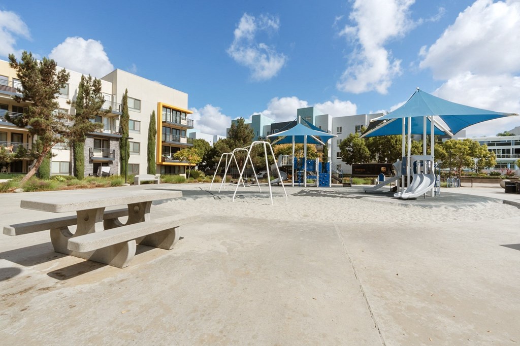 A playground with a blue canopy and a slide is surrounded by buildings.
