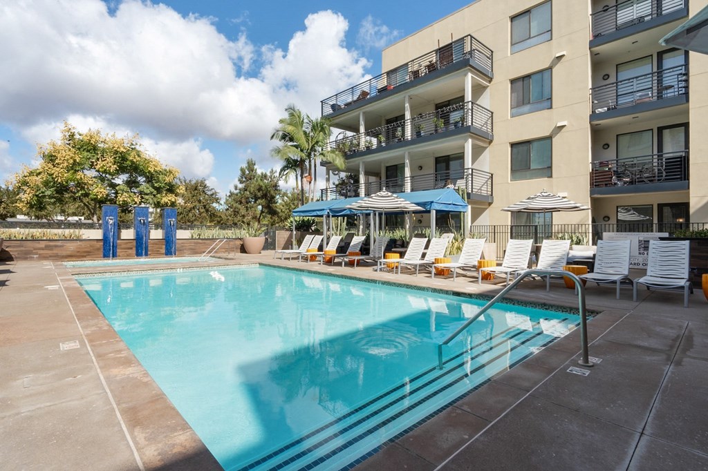 A large swimming pool in front of a building with sun loungers.