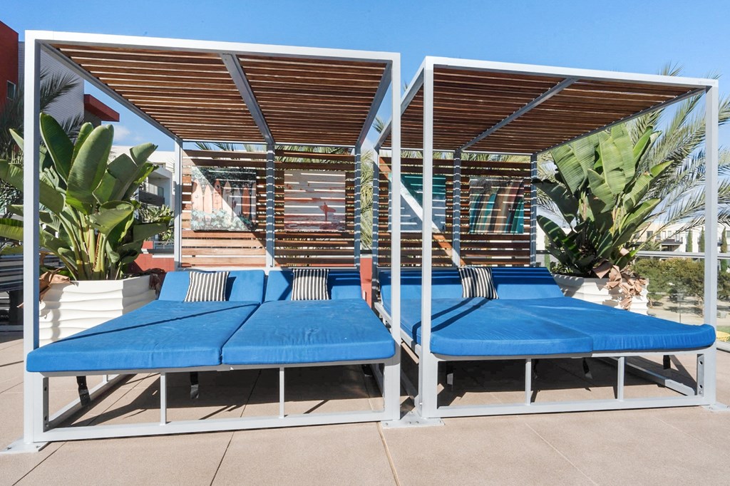 A blue and white daybed with a wooden roof is surrounded by green plants.