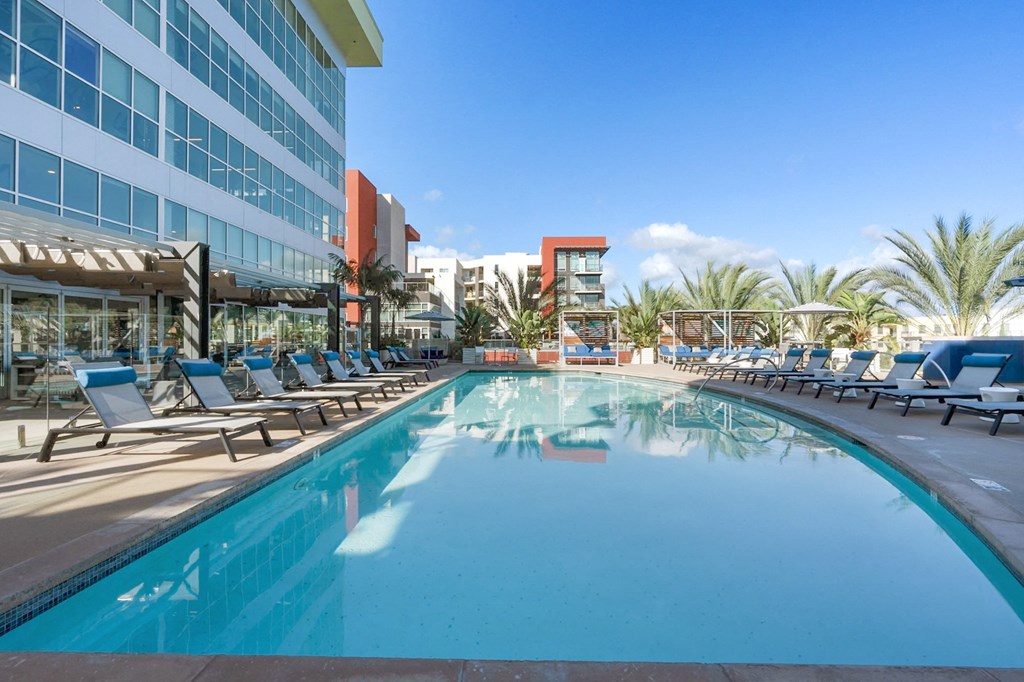 A large swimming pool with lounge chairs and a building in the background.