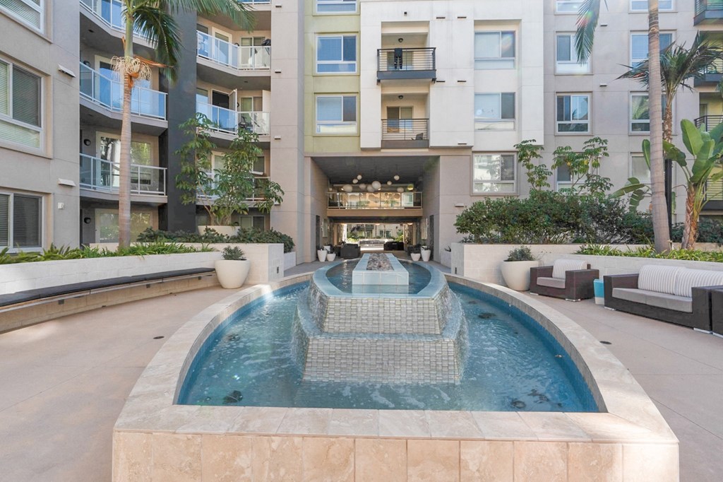 A modern pool with a waterfall in the middle of a courtyard surrounded by buildings.