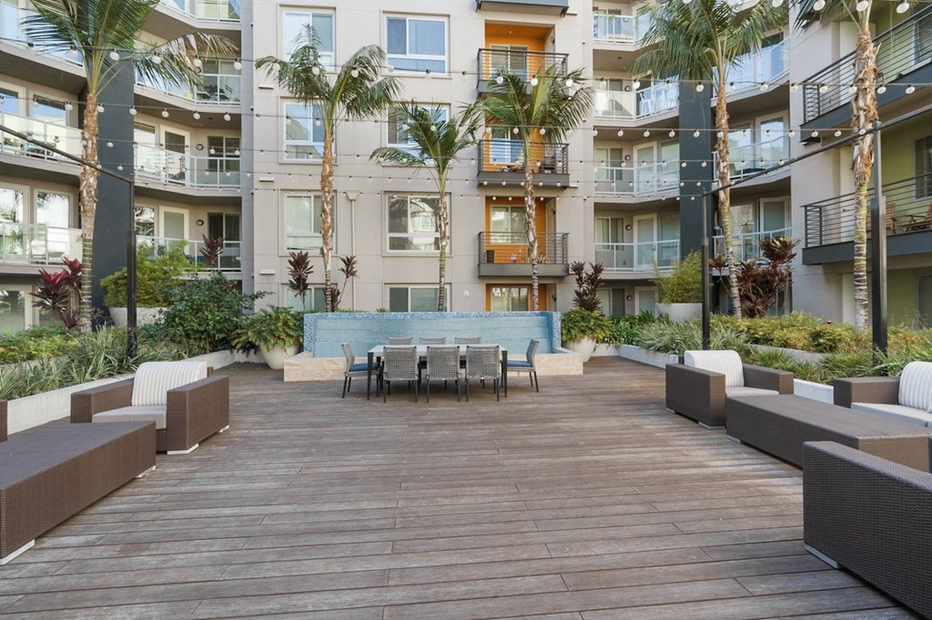 A wooden deck with a table surrounded by palm trees and balconies of apartment buildings.