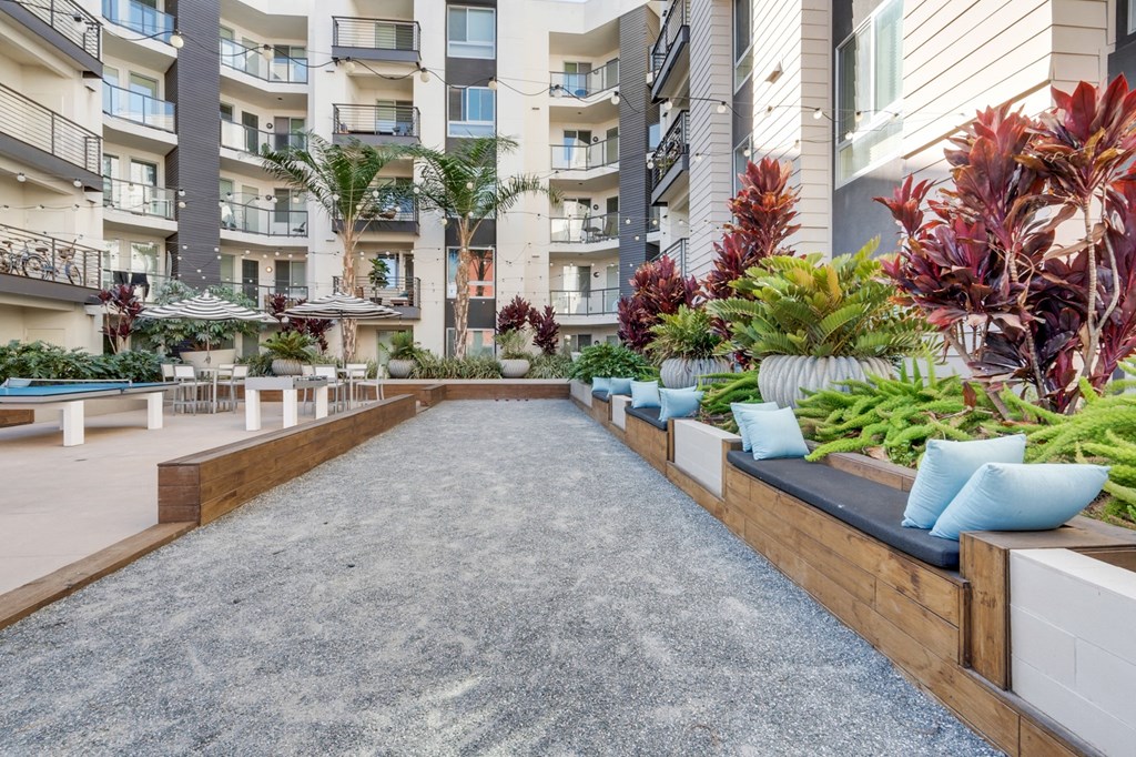 A long concrete walkway with a wooden bench on one side and a row of plants on the other.