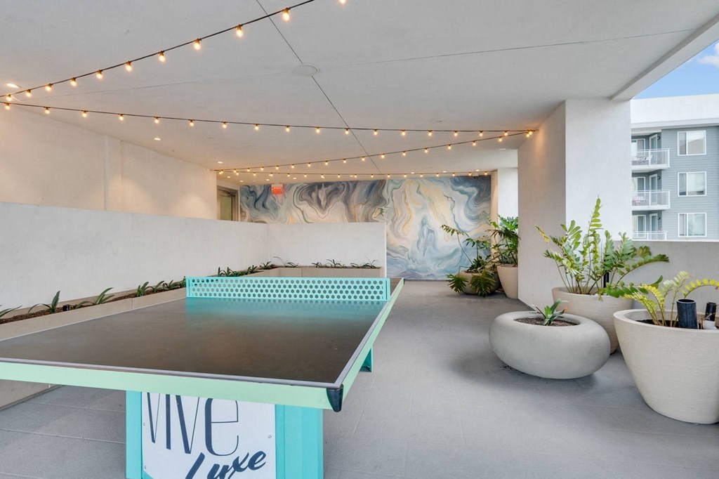 A ping pong table is in the middle of a room with plants on the side.