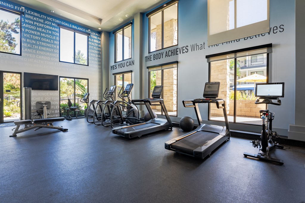a large fitness room with cardio equipment and windows