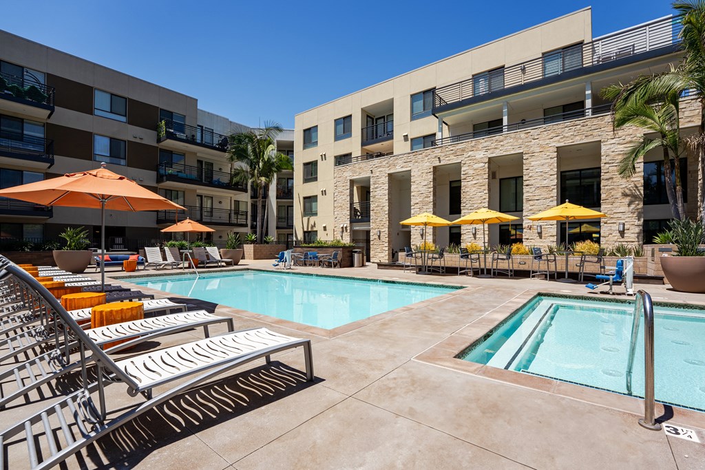 a swimming pool with lounge chairs and umbrellas in front of a building
