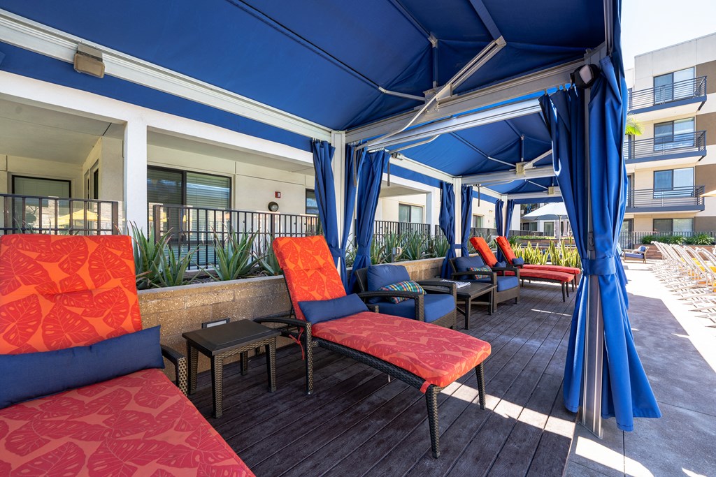 a seating area under a blue awning with red and blue chairs and blue curtains