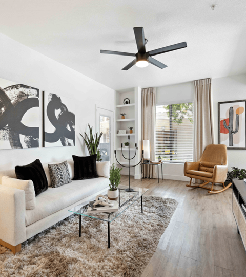 A living room with a white couch, a glass coffee table, a rocking chair, and a ceiling fan.