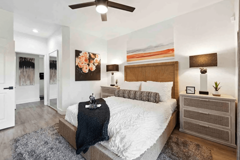 A bedroom with a large bed, a ceiling fan, and a painting on the wall.