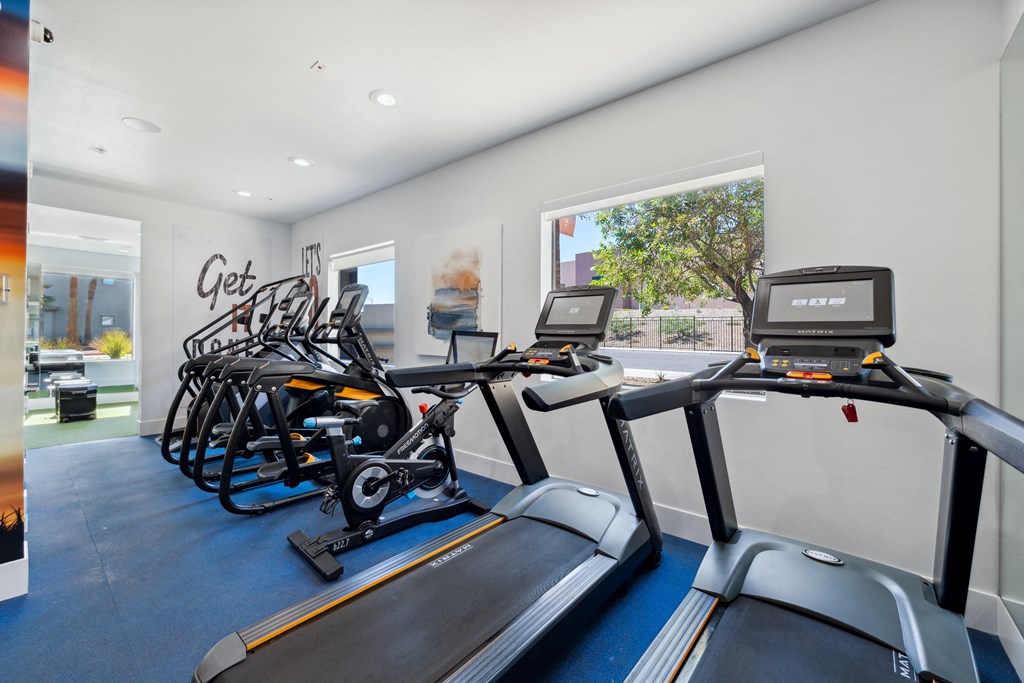 a gym with various cardio equipment on the floor and a window