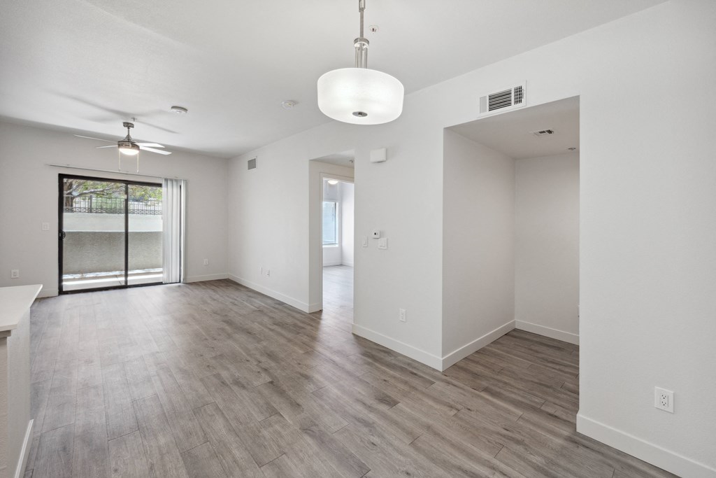 the living room and dining room of an apartment with white walls and wood flooring