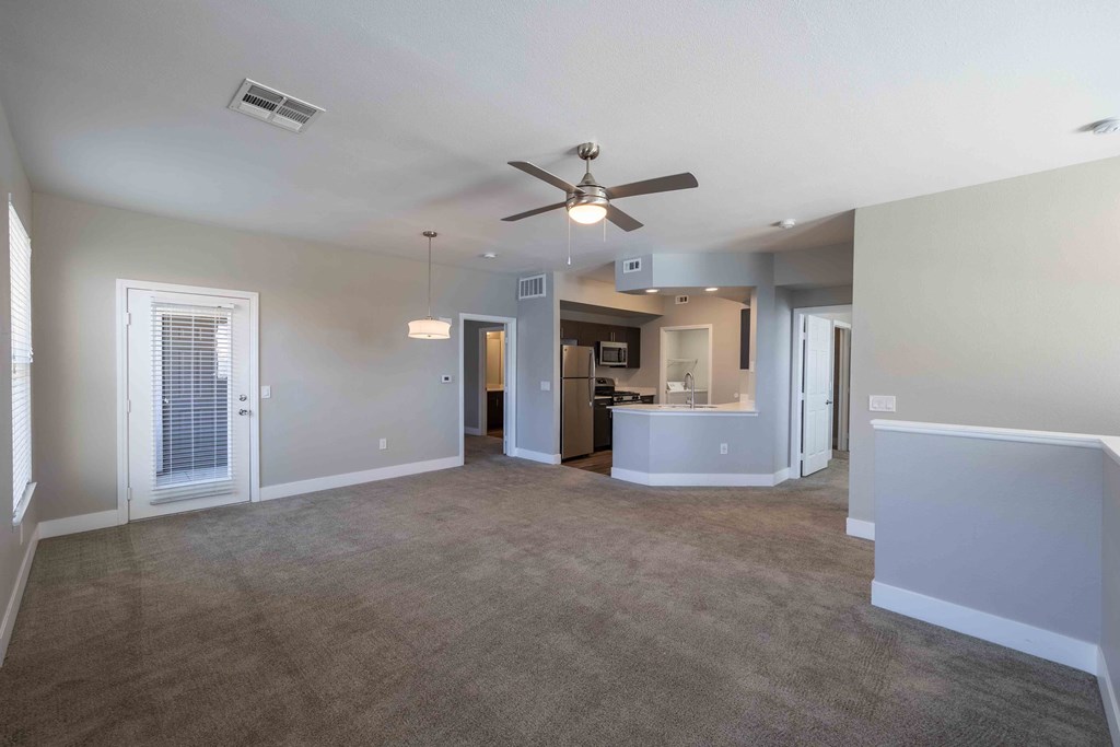 an empty living room with a ceiling fan and a kitchen