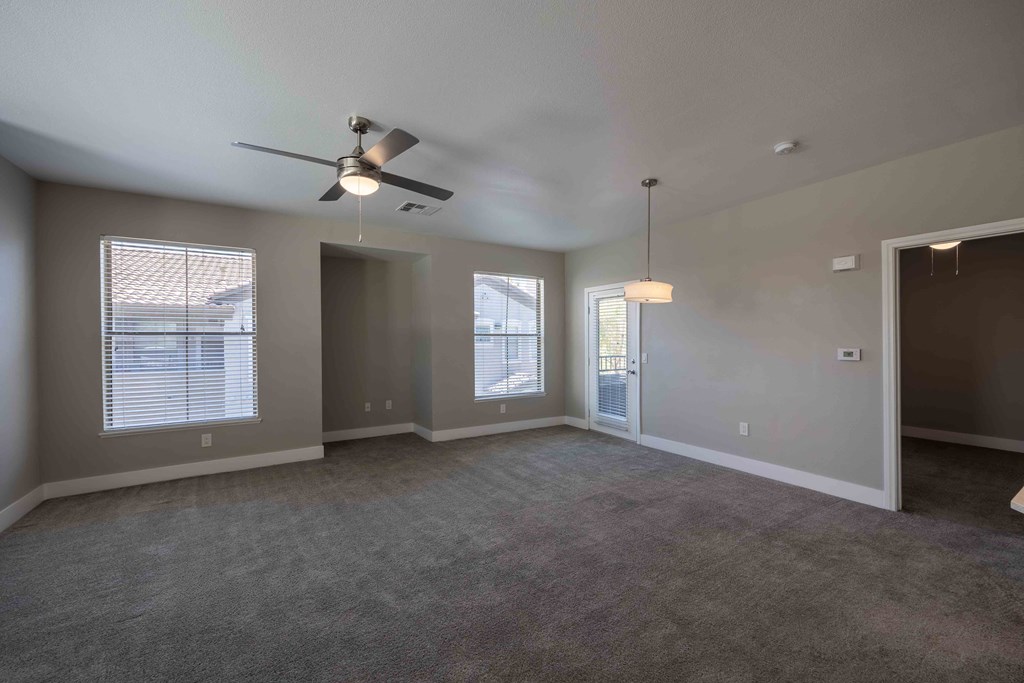 an empty living room with a ceiling fan and window