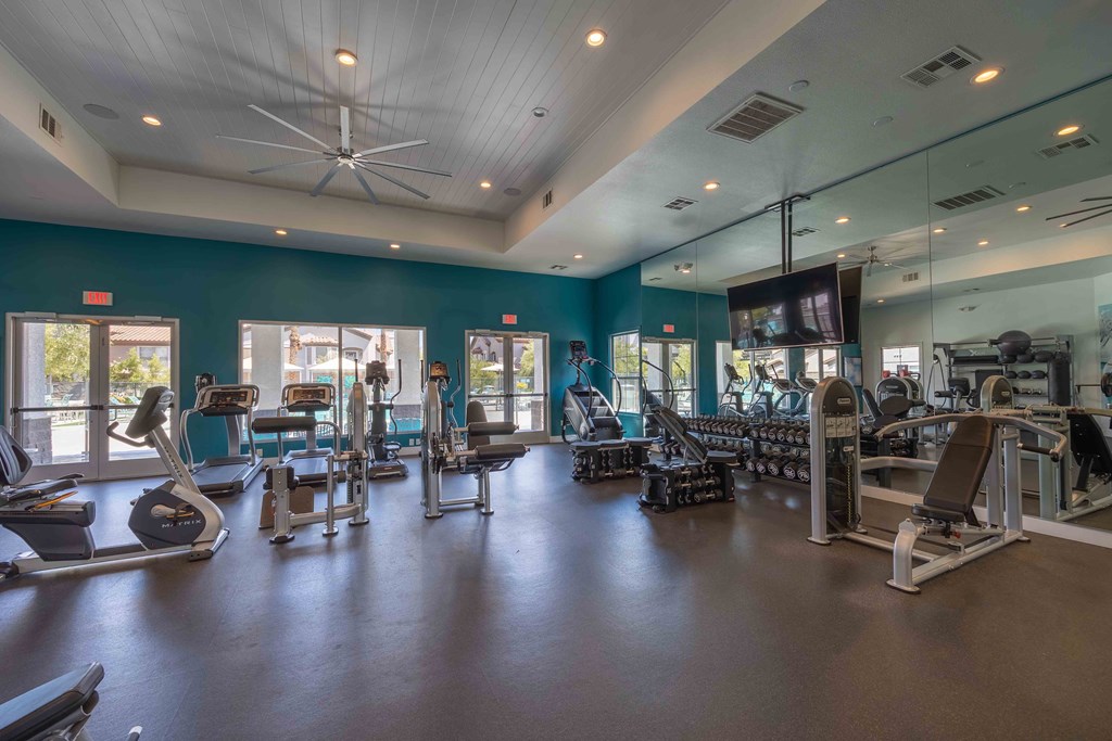 a gym with cardio equipment and weights in a building with windows
