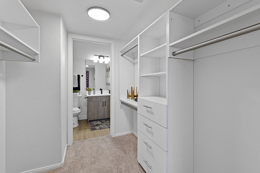 a walk in closet with white cabinets and a bathroom with a toilet and a sink