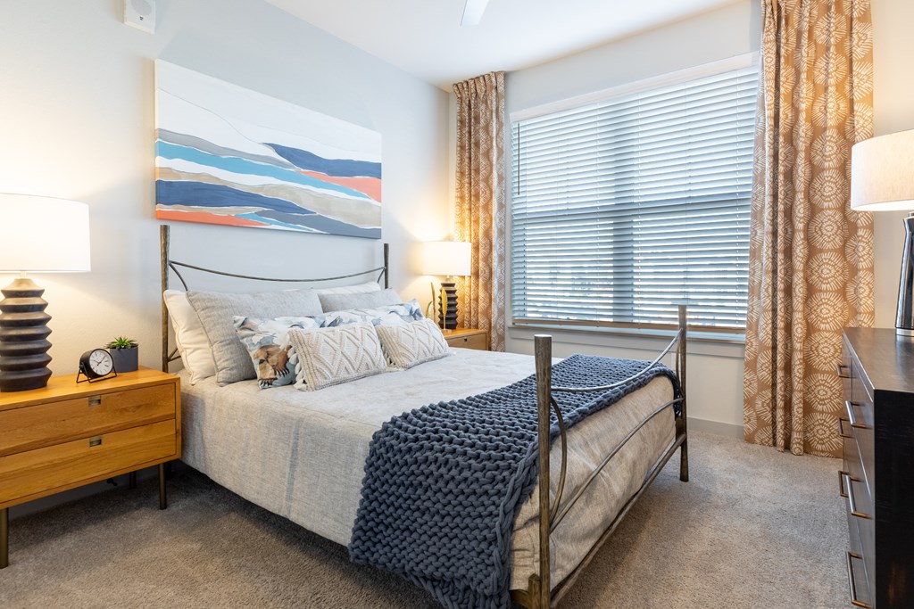 a bedroom with a bed and a large window with blinds and a dresser