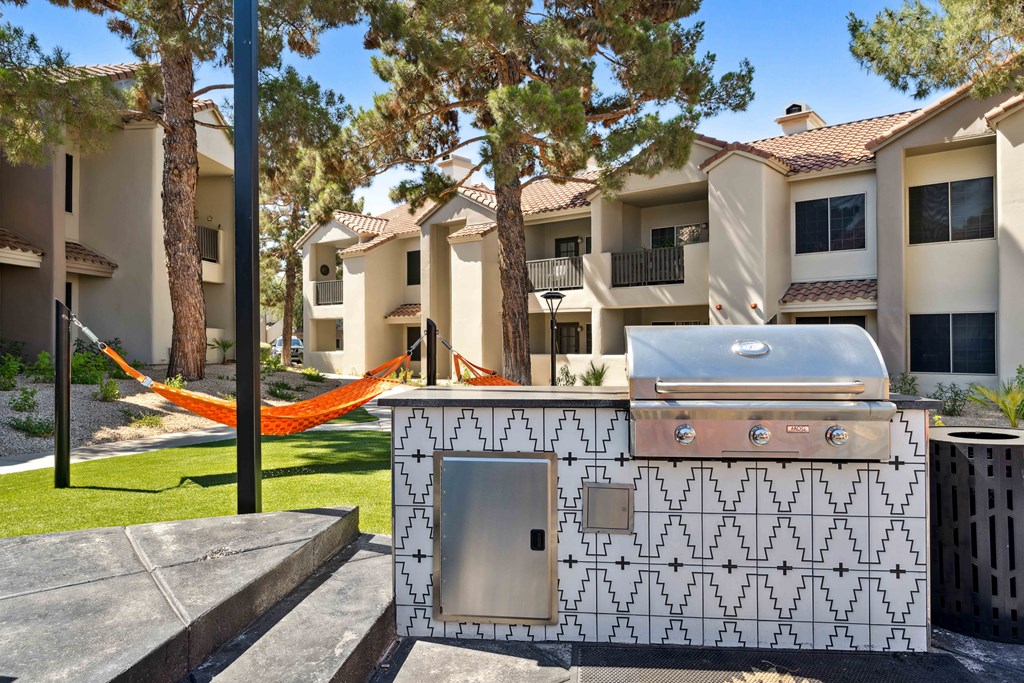 an outdoor barbecue grill with a hammock and apartment buildings in the background