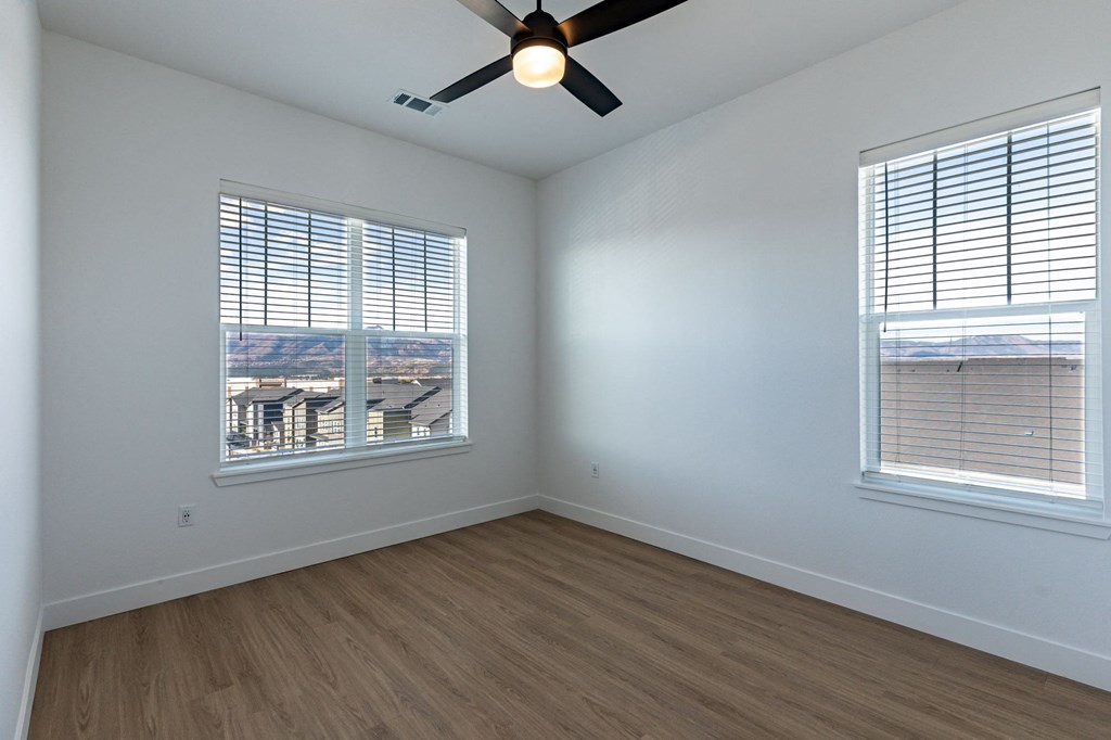 an large bedroom with two windows and a ceiling fan