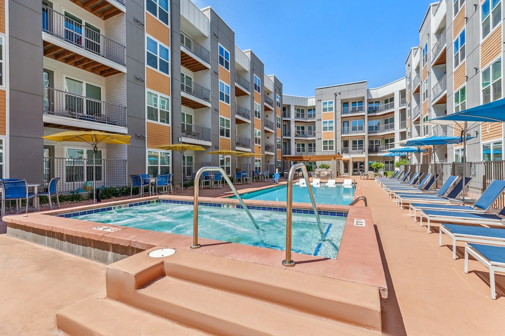 a pool with lounge chairs and umbrellas in front of an apartment building