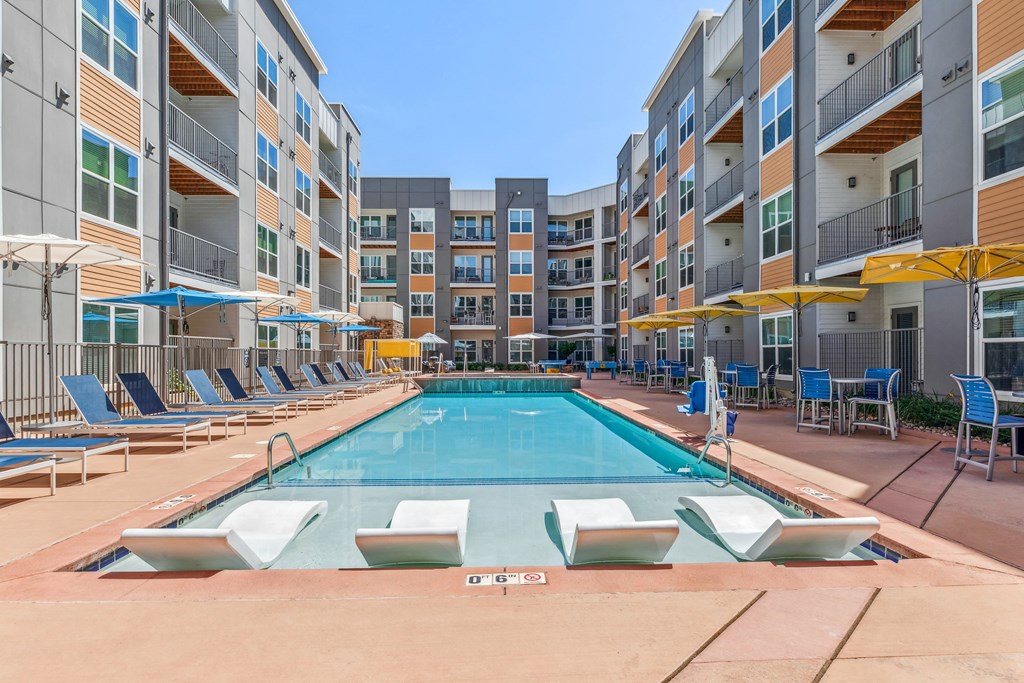 a swimming pool with chaise lounge chairs and umbrellas in front of an apartment building