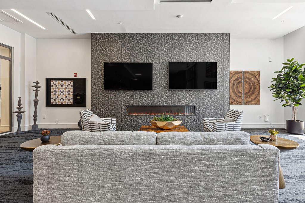 a living room with a gray couch and two televisions on the wall