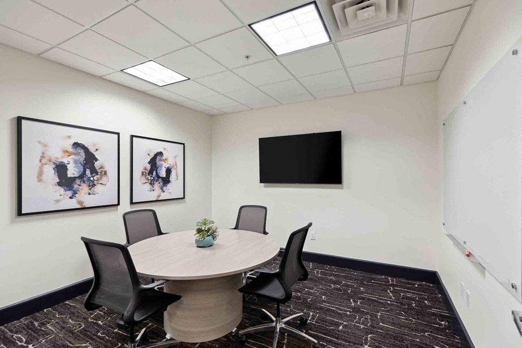 a meeting room with a round table and chairs and a flat screen tv on the wall