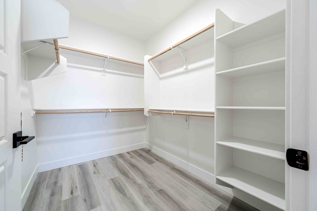 a walk in closet with white walls and wooden floors