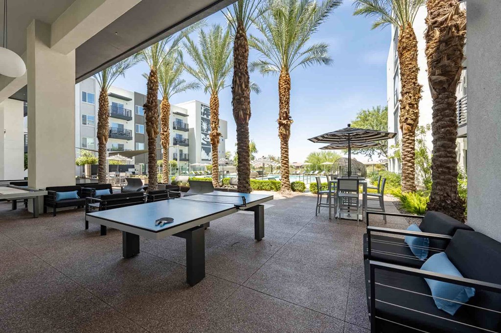 a patio with a ping pong table and chairs with palm trees in the background