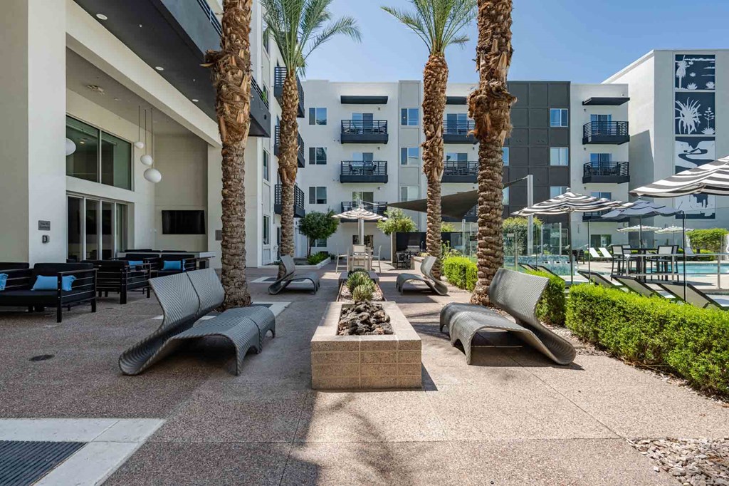 a patio with lounge chairs and a fire pit in front of a slate scottsdale apartment building