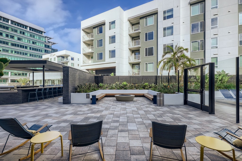 a patio with chairs and a fire pit in front of an apartment building