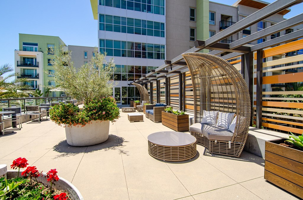 a patio with a swing chair and potted plants in front of a building