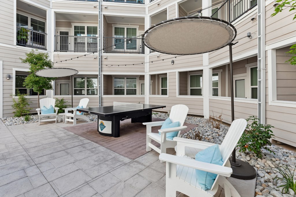 a patio with a ping pong table and lounge chairs