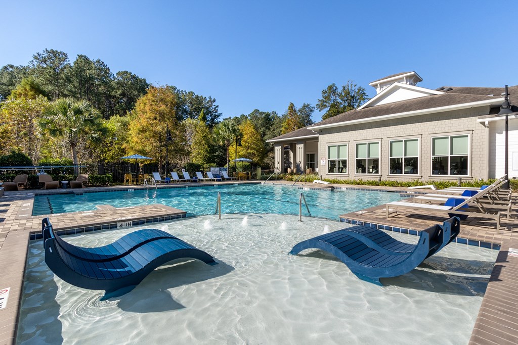 our resort style swimming pool with lounge chairs and a building in the background