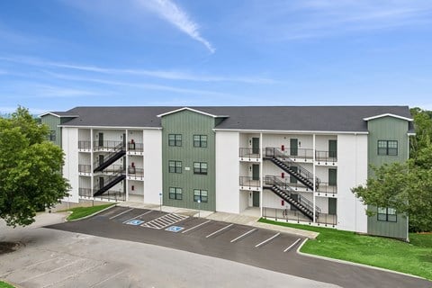 A large white and green apartment complex with a parking lot in front.