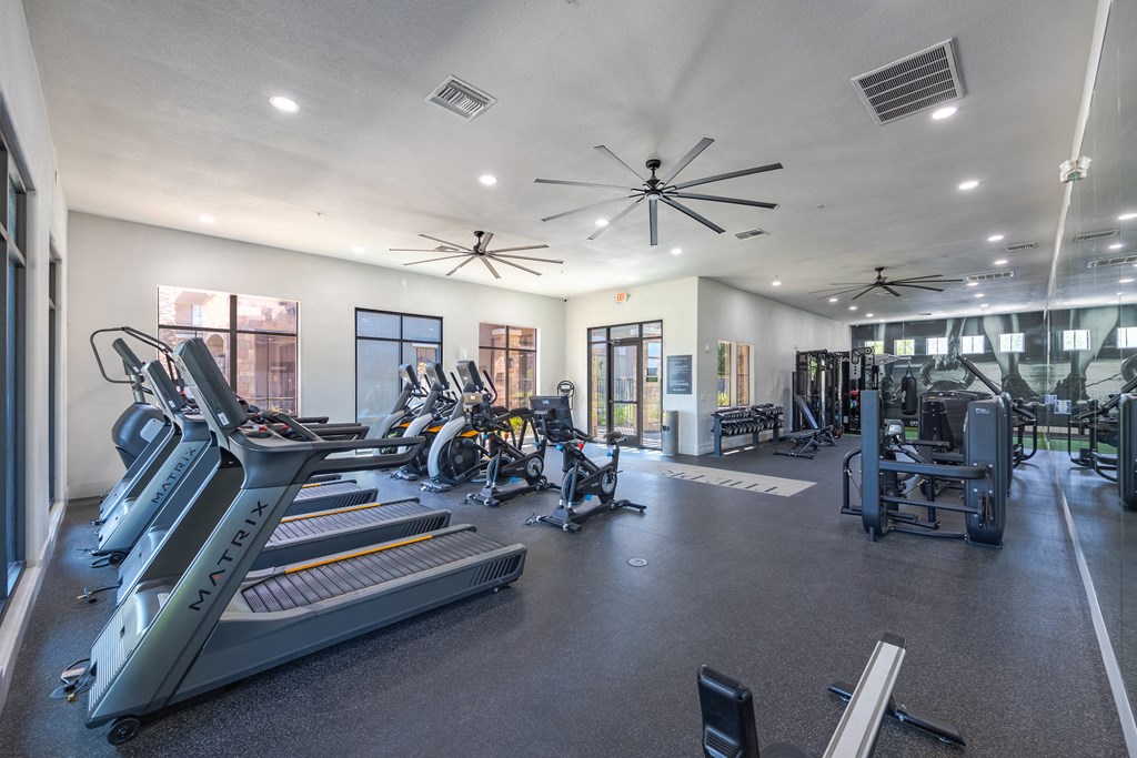 a spacious fitness center with cardio equipment and windows