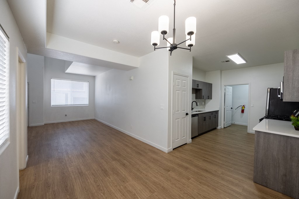 an empty living room with a kitchen in the background