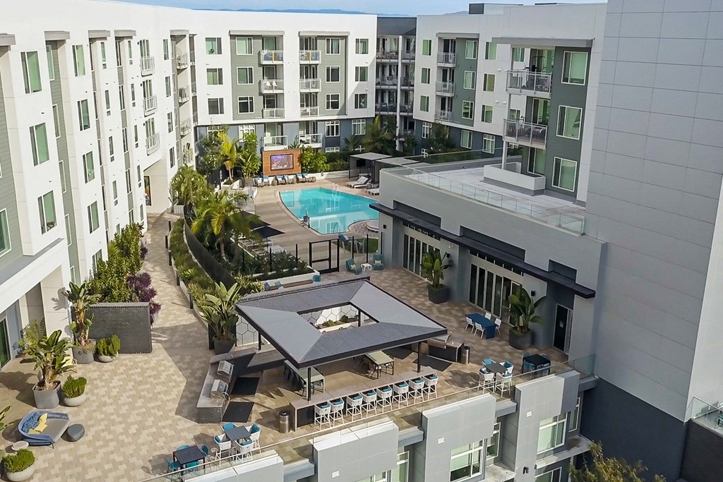 A large outdoor pool area with a table and chairs is surrounded by apartment buildings.