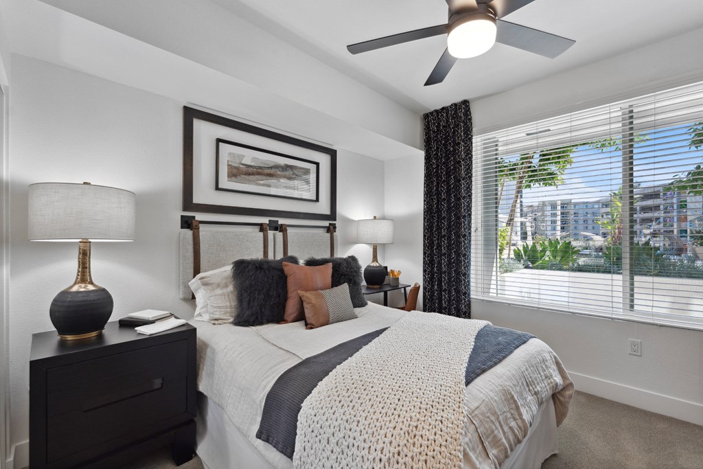 A bedroom with a large bed, a ceiling fan, and a window with blinds.
