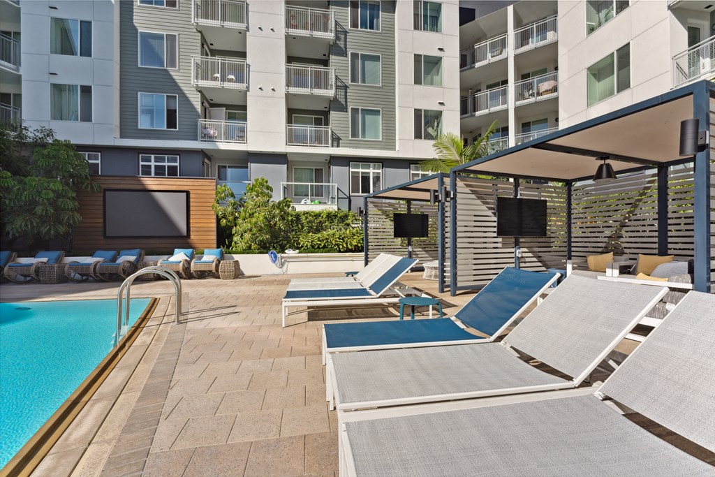 A pool area with sun loungers and a building in the background.