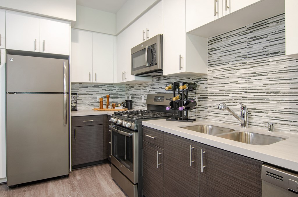 A modern kitchen with a stainless steel refrigerator and a stone backsplash.